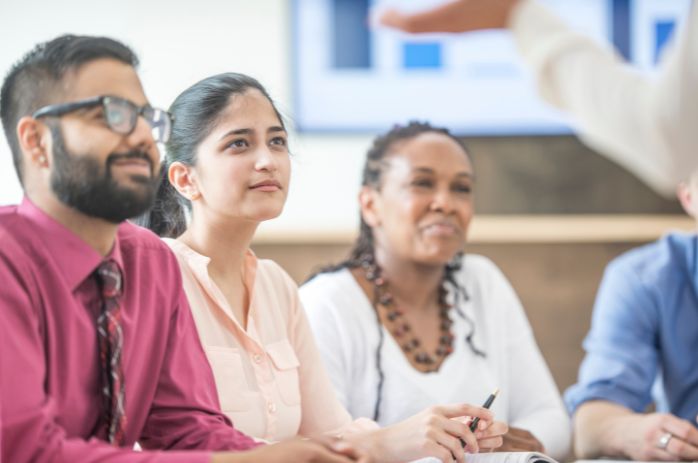 Three people sitting listening to a speaker delivering training.