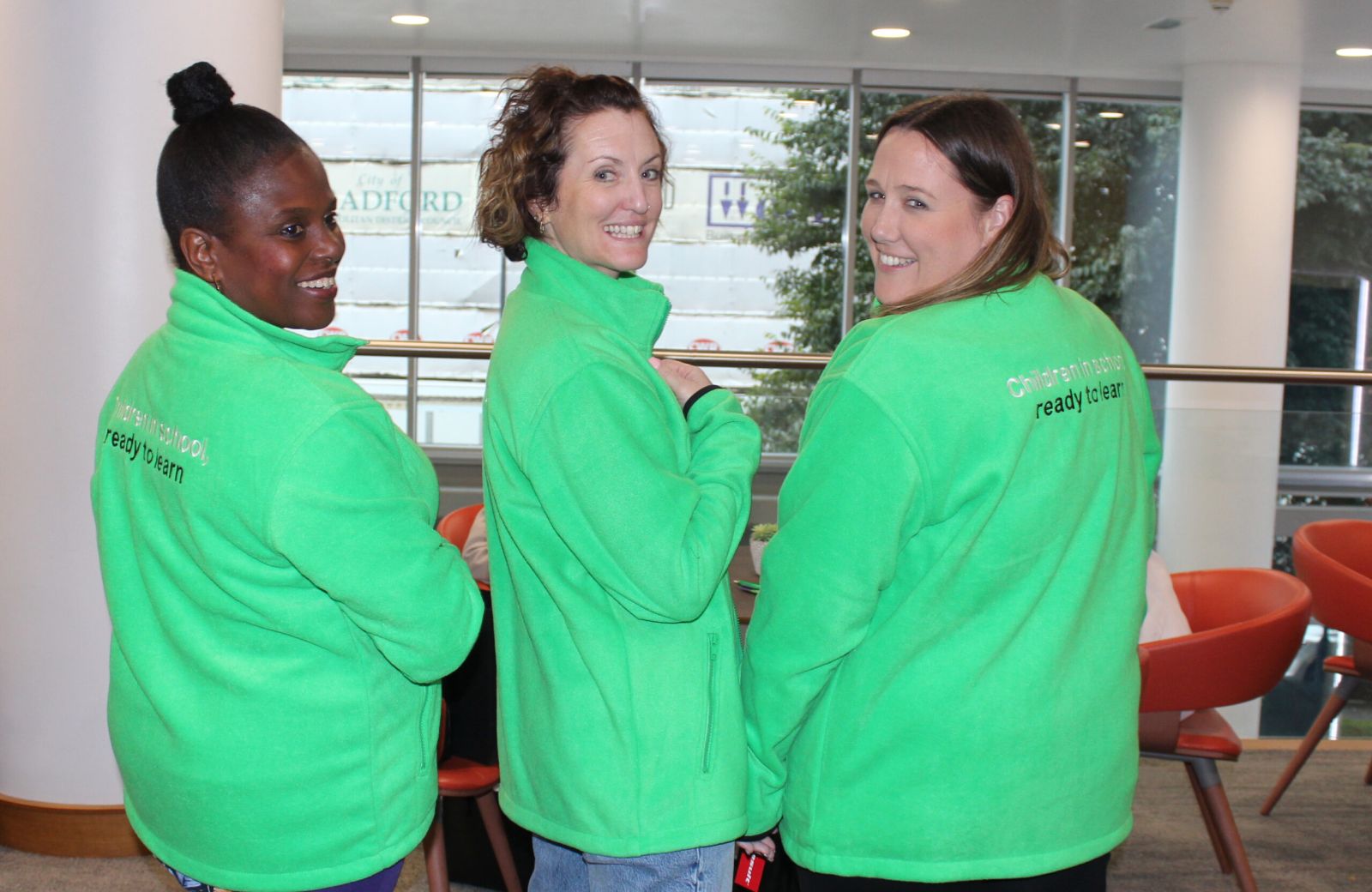 Three School-Home Support practitioners stand with their back to the camera, turning around to smile at the camera.