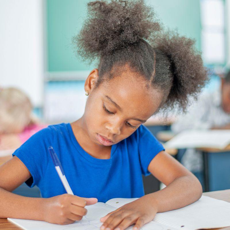 A child in a classroom writing in a workbook.